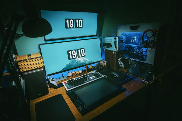 A sleek gaming desk setup featuring dual monitors, keyboard, and gaming PC in a dimly lit home office.