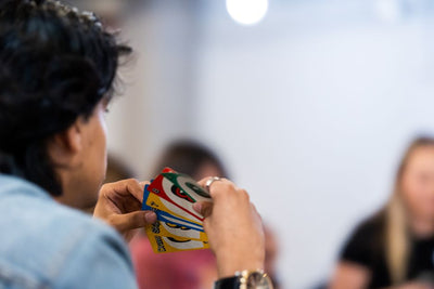 A person intently holds a variety of colorful game cards during indoor gathering.