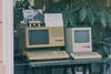Retro Apple computers with keyboards displayed in a Tokyo store window, showcasing early tech design.