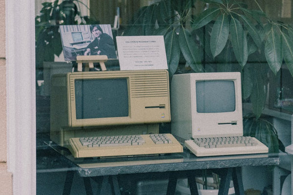 Retro Apple computers with keyboards displayed in a Tokyo store window, showcasing early tech design.
