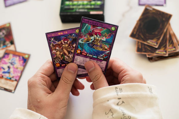 Hands holding Yu-Gi-Oh! trading cards in a dynamic gaming setup with blurred background.