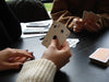 Three people playing a card game indoors, showing a hand of playing cards.