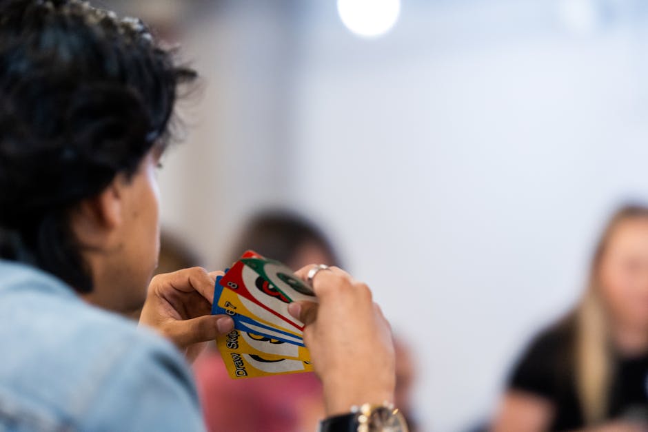 A person intently holds a variety of colorful game cards during indoor gathering.
