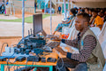 Technician managing electrical and computer setup at an outdoor event with attentive audience.
