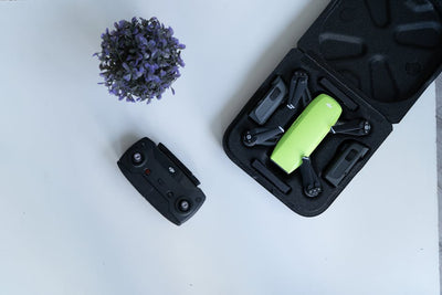 Top view of a compact green drone, controller, and lavender flowers on a white surface.