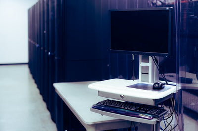 Contemporary computer with black screen placed on stand near row of server steel racks in data center