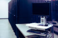 Contemporary computer with black screen placed on stand near row of server steel racks in data center