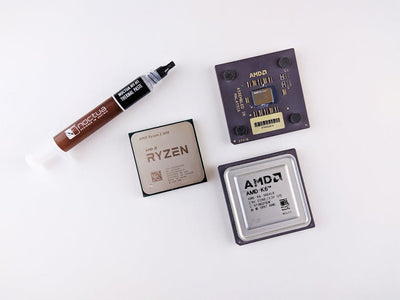 High-angle view of AMD processors and Noctua thermal paste on a white surface.