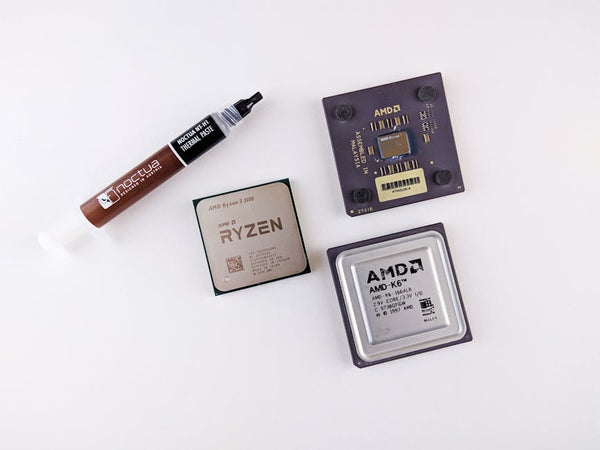 High-angle view of AMD processors and Noctua thermal paste on a white surface.