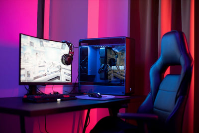 A sleek gaming setup featuring a high-end PC, widescreen monitor, and ergonomic chair lit by neon lights.